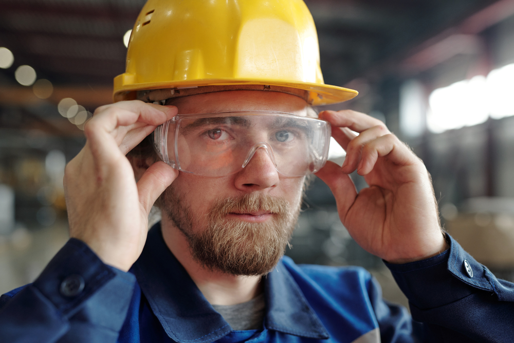 factory worker with beard adjusting protective goggles in industry who no longer has to hassle with eyeglasses stuck under his goggles